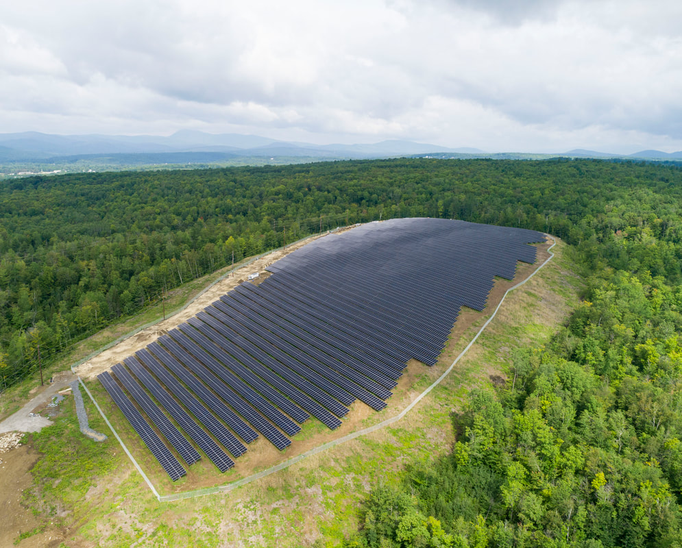 An aerial shot of one of the Farmington solar fields, surrounded by green forests.