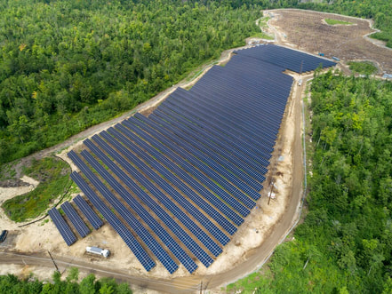 A shot of the partially finished solar field, with rows of solar panels stretching across the frame, and a cleared dirt lot behind them.