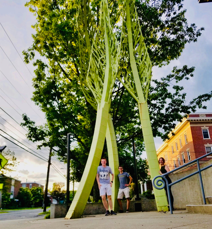 An image of the three student interns standing beneath a tall, green sculpture that resembles a tree.