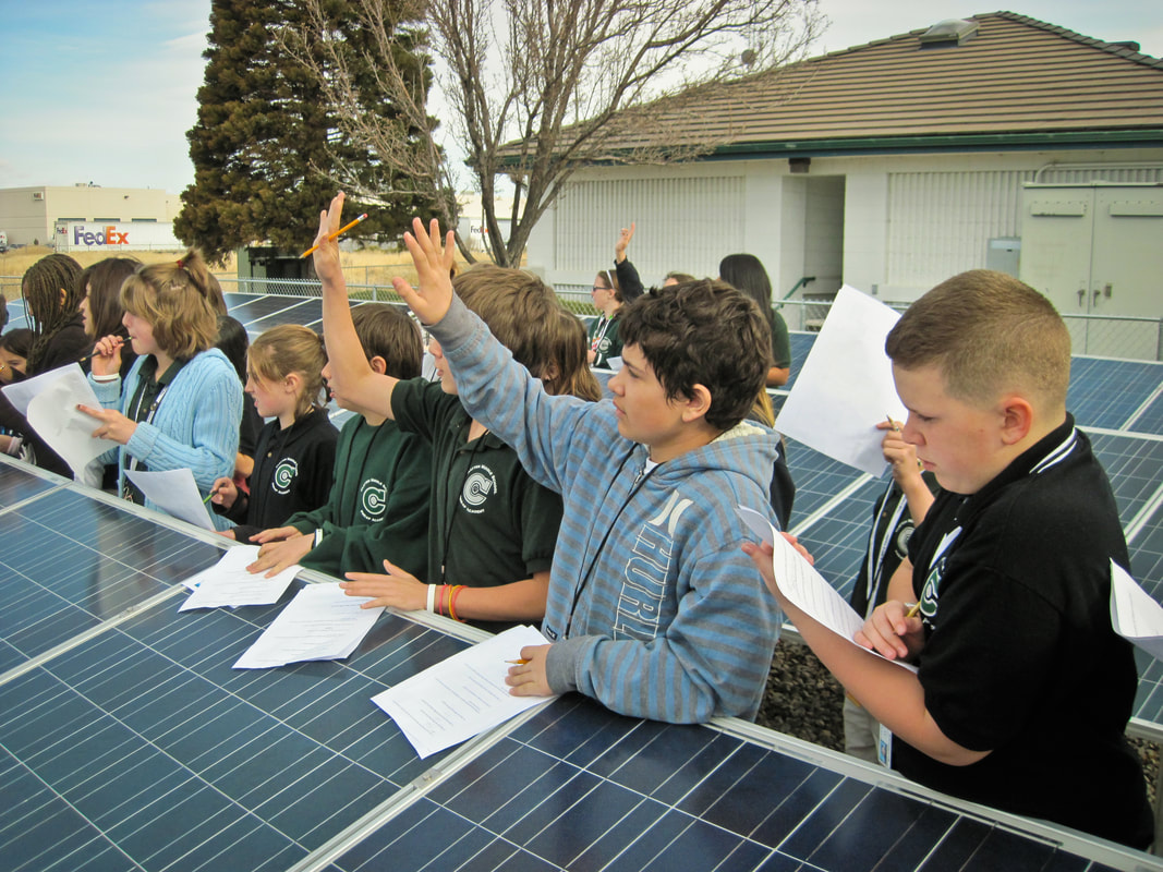 An image of a group of schoolchildren holding pencils and paper, leaning on rows of small solar panels.
